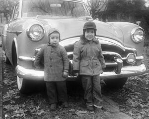 Two little boys standing in front of a 1953 Packard coupe. Iowa, USA 1955. Scanned film with grain.