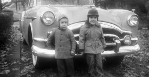 Two little boys standing in front of a 1953 Packard coupe. Iowa, USA 1955. Scanned film with grain.